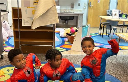 3 students wearing spiderman costumes sitting on the floor